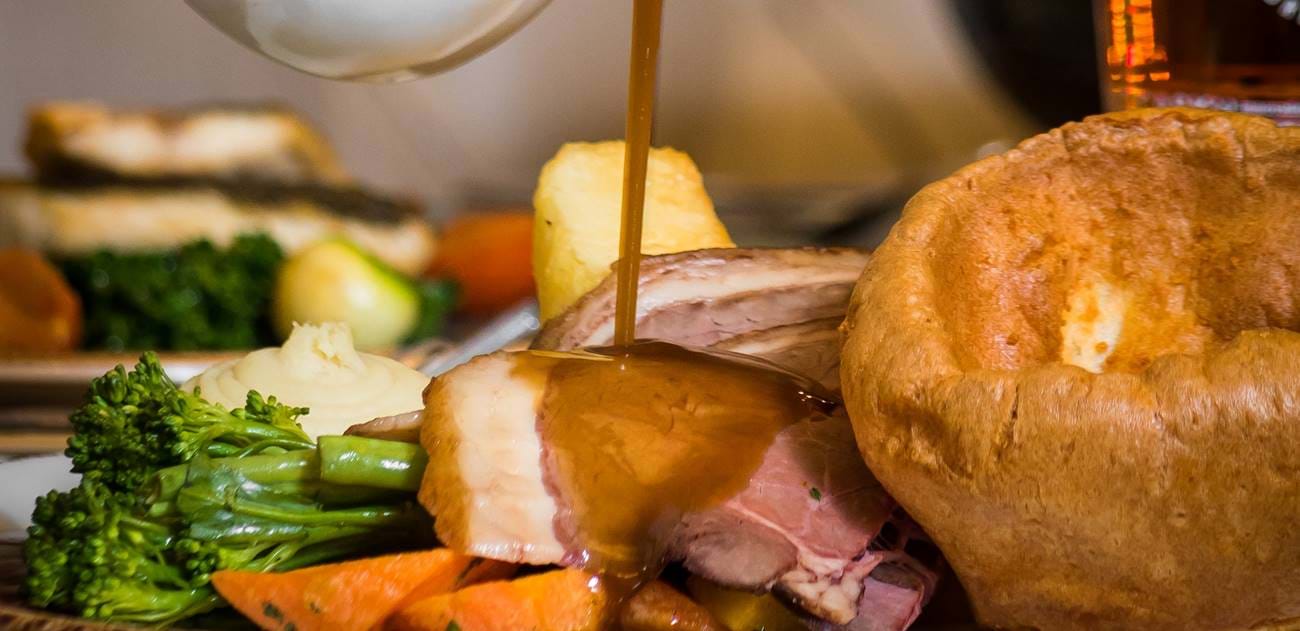 roast dinner with gravy being poured over the top big yorkshire pudding